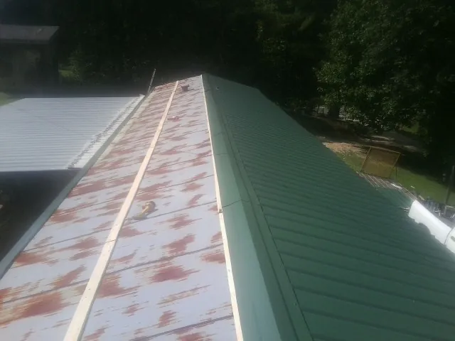 Old rusted panels beside newly installed green metal roofing — Wind Damage Roof Repair by Roofing Brothers in Pelham