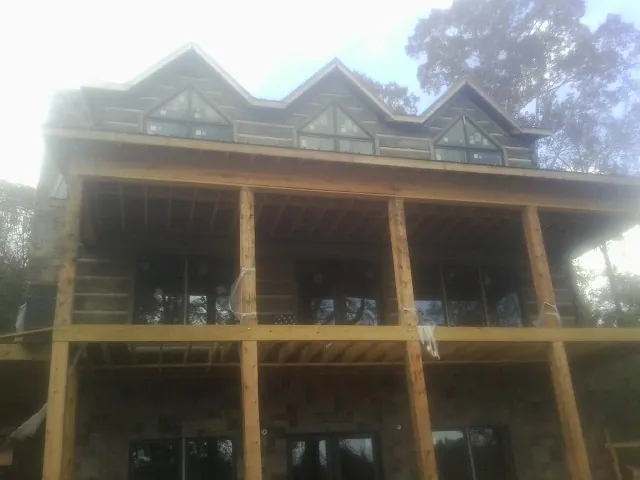 Dormers and porch framing on a large log home under construction — Roof Coating work by our crew in Pelham