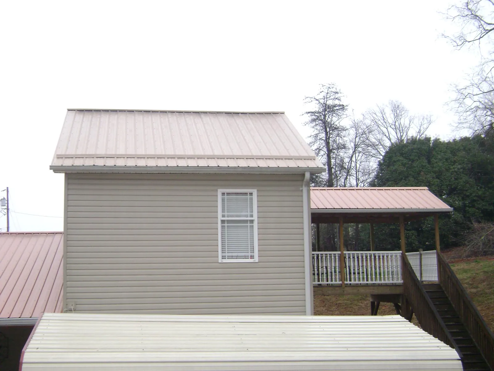 Tan metal roofs on a two story addition and attached porch, from a Roof Replacement job in Pelham